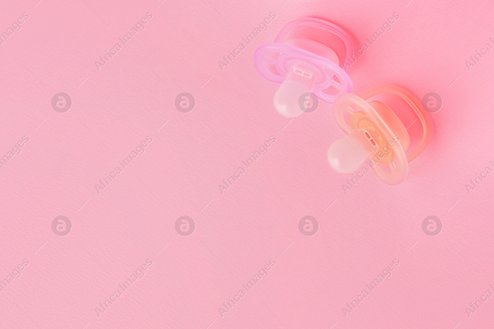 Photo of New baby pacifiers on pink background, flat lay. Space for text