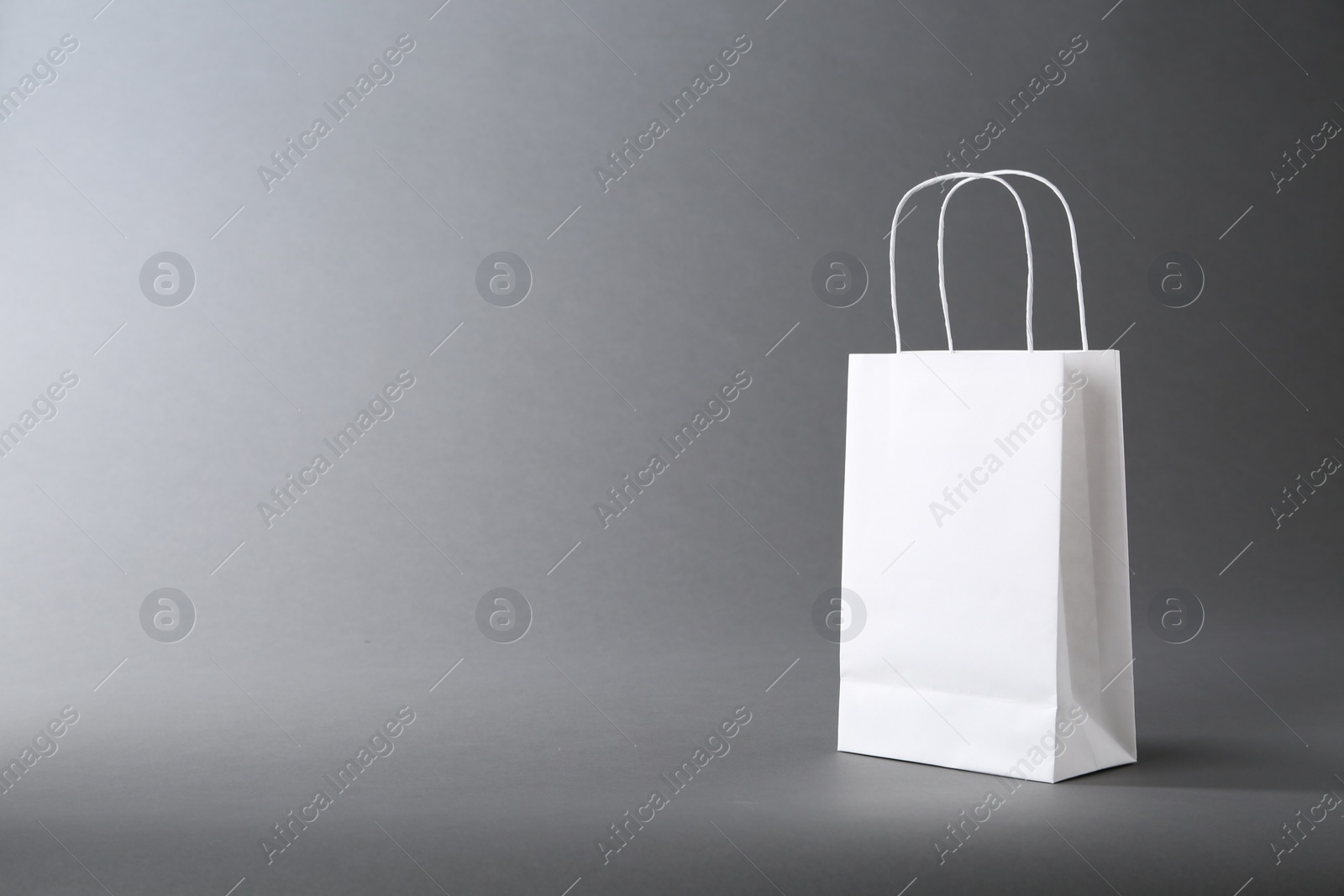 Photo of One white paper bag on grey background, space for text. Mockup for design