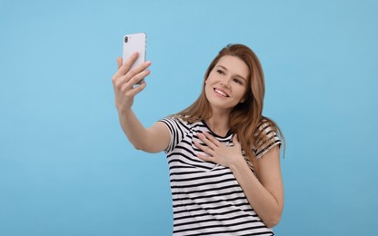 Beautiful woman taking selfie on light blue background