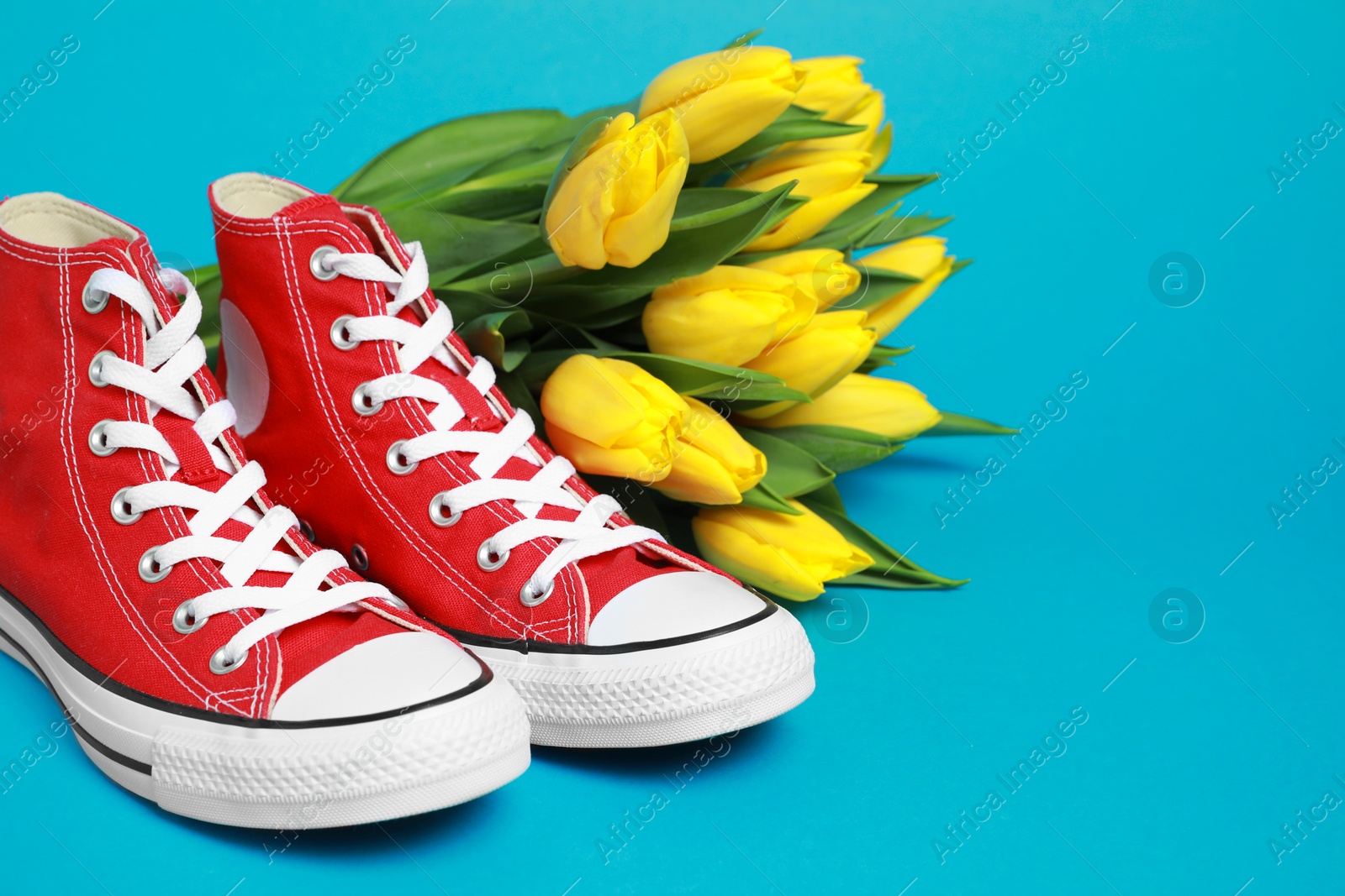 Photo of Pair of new stylish red sneakers and beautiful tulips on light blue background. Space for text