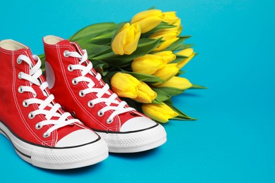 Photo of Pair of new stylish red sneakers and beautiful tulips on light blue background. Space for text