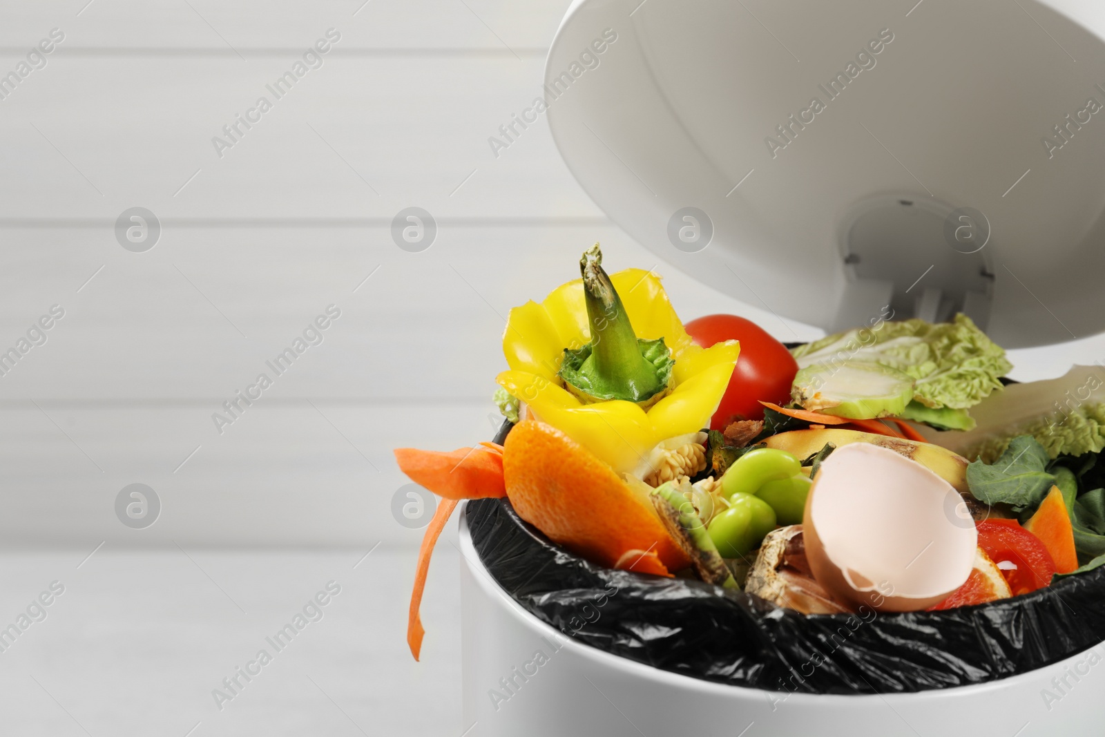 Photo of Natural garbage in trash bin on light background, closeup with space for text. Composting of organic waste