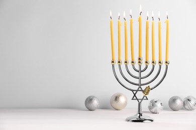 Photo of Hanukkah celebration. Menorah with burning candles and holiday ornaments on white wooden table, space for text