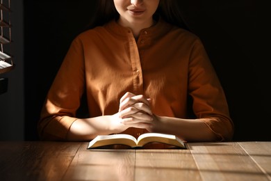 Photo of Religious woman praying over Bible at wooden table indoors, closeup