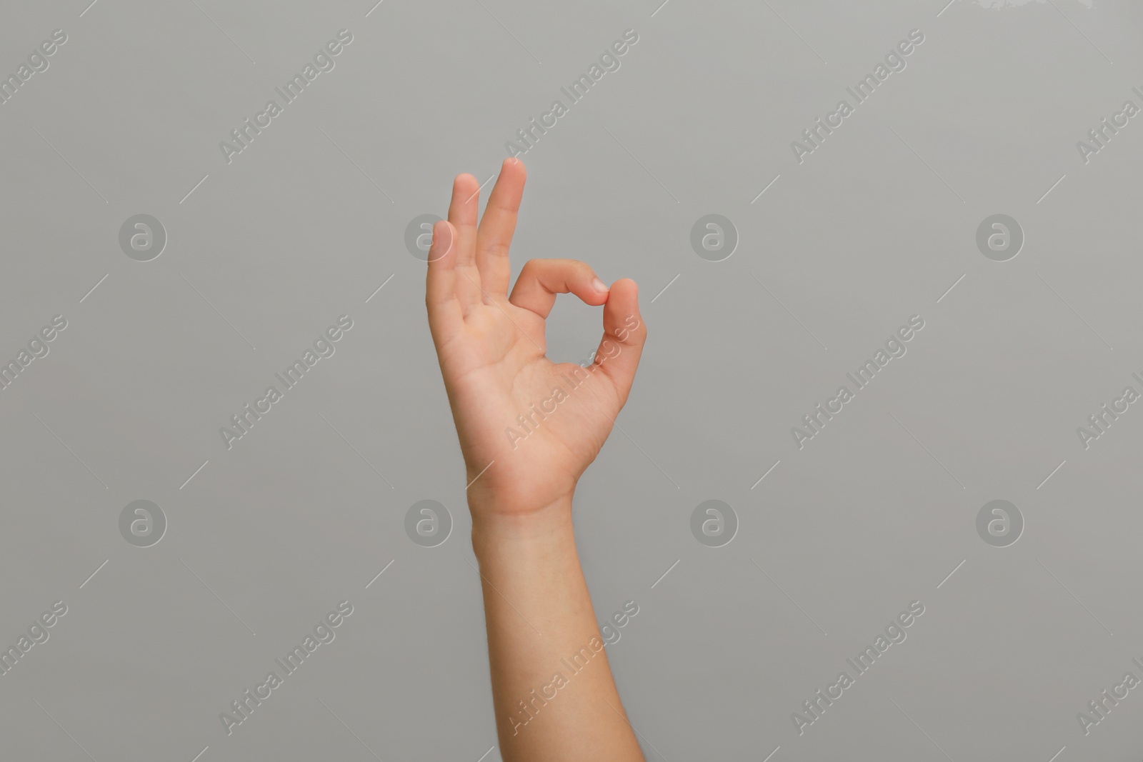 Photo of Teenage boy showing ok gesture on light grey background, closeup