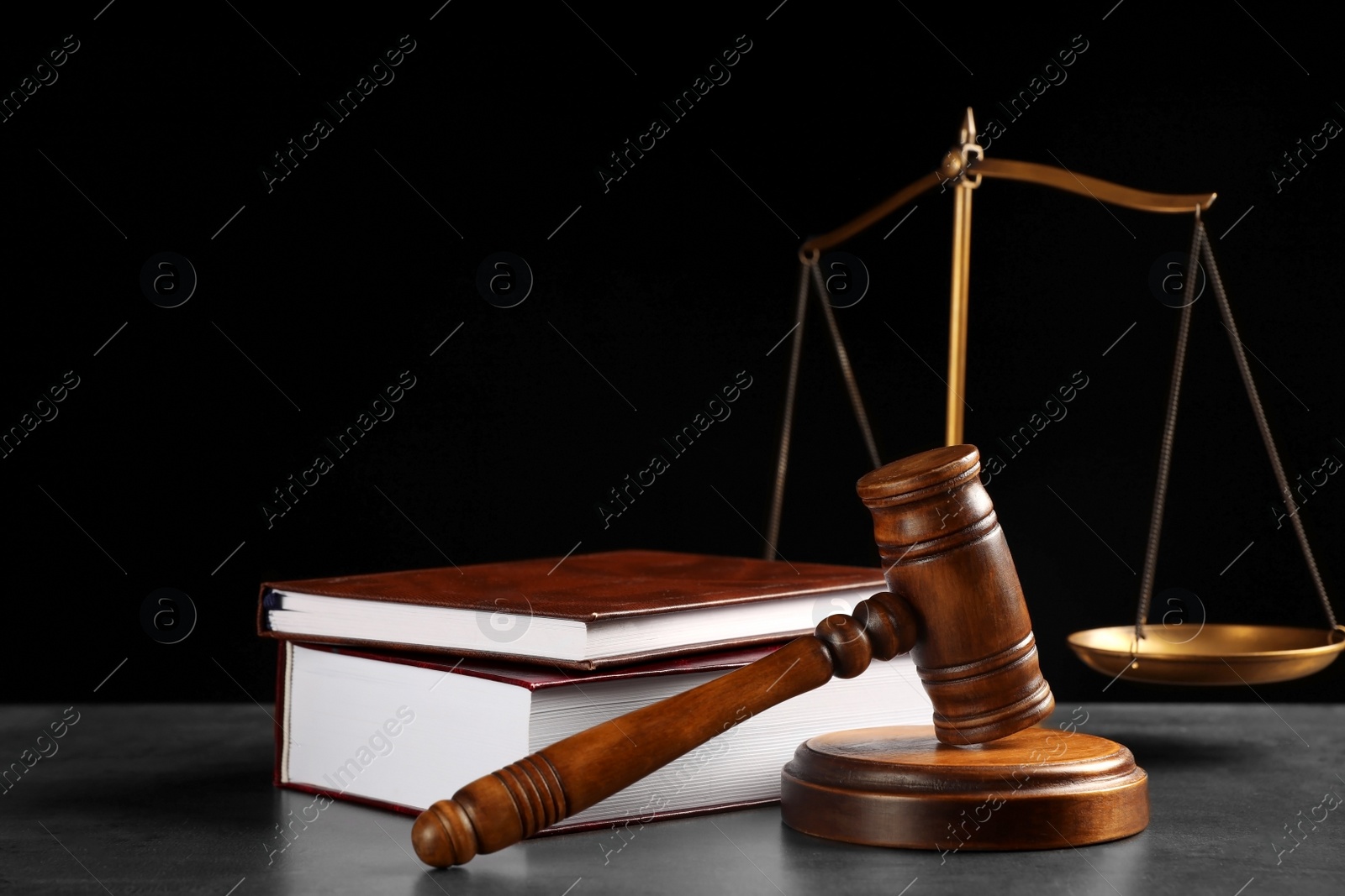 Photo of Judge's gavel, books and scales on grey table against black background. Criminal law concept