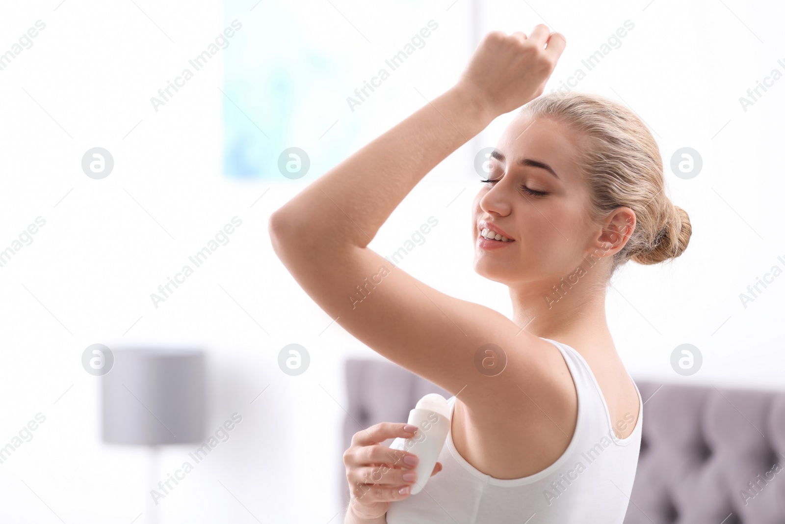 Photo of Beautiful young woman applying deodorant in bedroom. Space for text