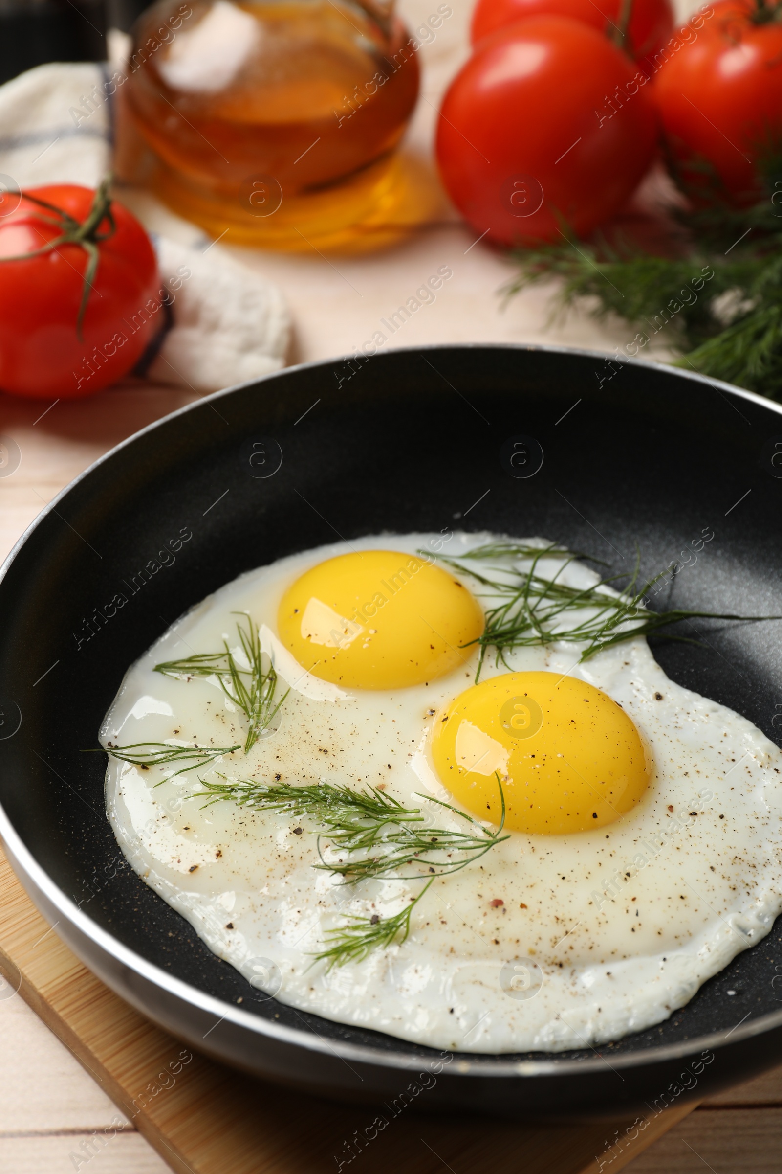 Photo of Frying pan with tasty cooked eggs, dill and other products on light wooden table, closeup