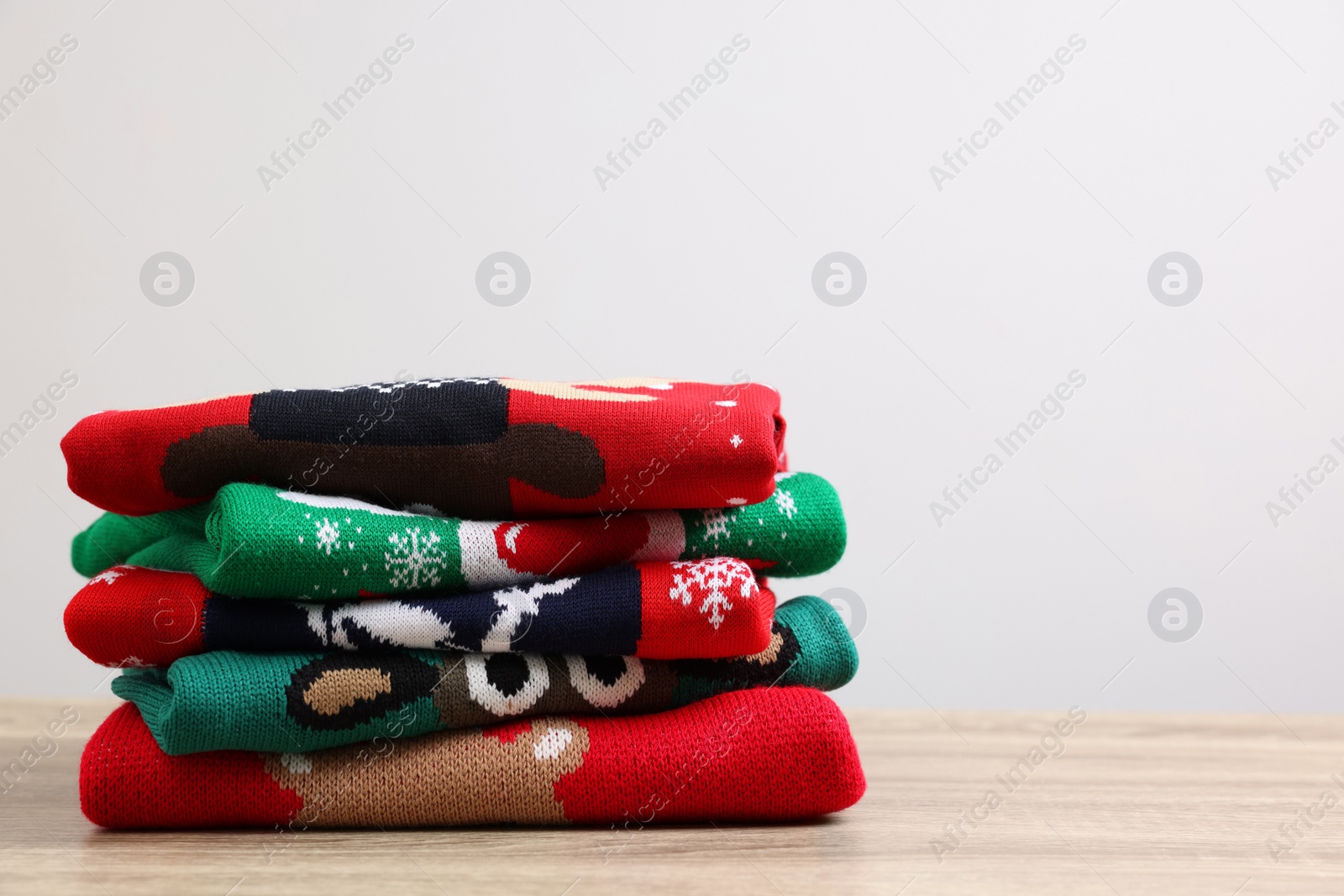Photo of Stack of different Christmas sweaters on wooden table against light background. Space for text