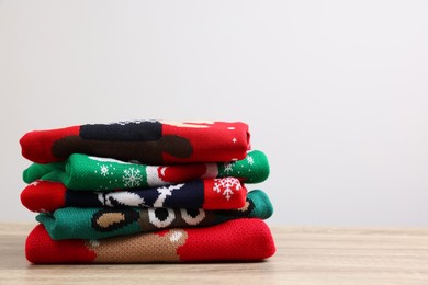 Stack of different Christmas sweaters on wooden table against light background. Space for text