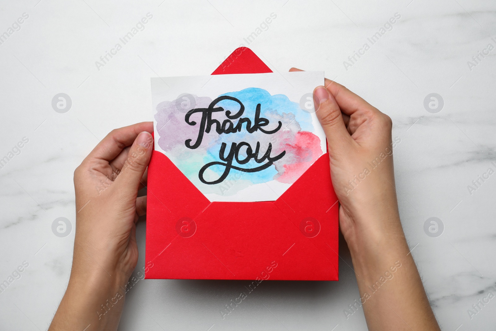 Photo of Woman holding envelope and card with phrase Thank you at white marble table, top view