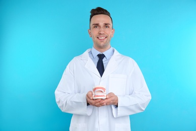Photo of Male dentist holding jaws model on color background