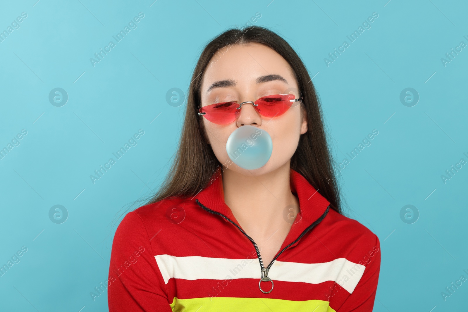 Photo of Beautiful young woman blowing bubble gum on light blue background