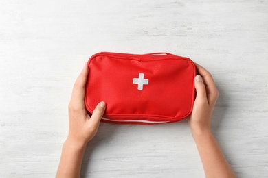 Photo of Woman holding first aid kit on wooden background, top view