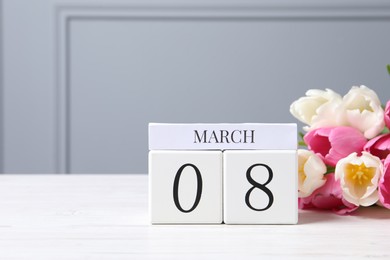 Photo of International Women's day - 8th of March. Wooden block calendar and beautiful flowers on white table, space for text