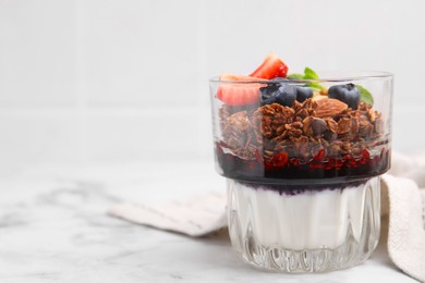 Tasty granola with berries, jam and yogurt in glass on white marble table, space for text