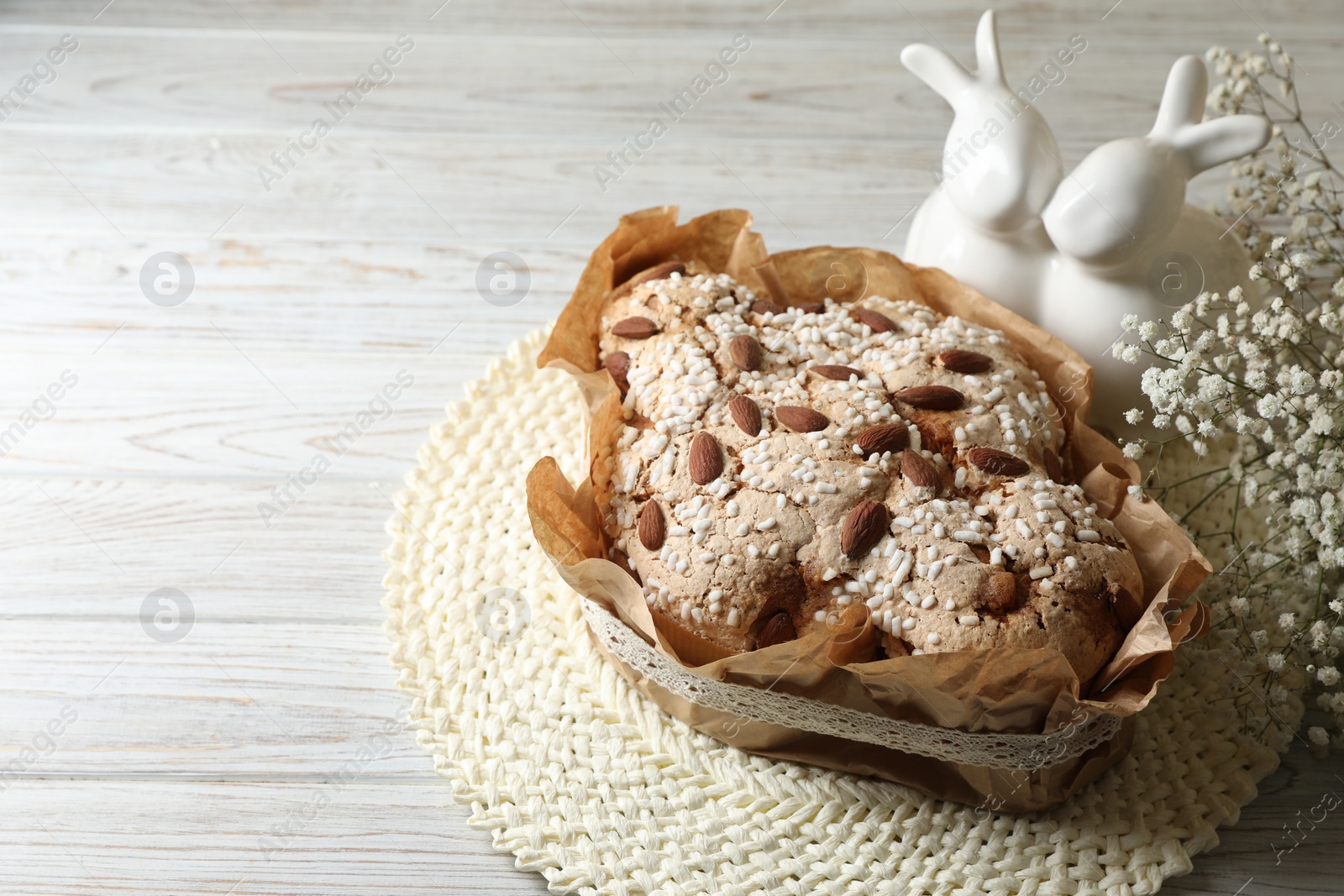 Photo of Delicious Italian Easter dove cake (traditional Colomba di Pasqua) and festive decor on white wooden table, space for text