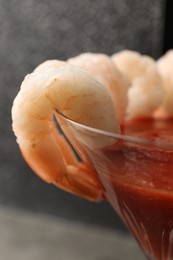 Photo of Tasty shrimp cocktail with sauce in glass on grey background, closeup