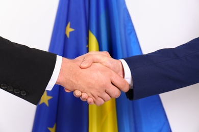 Men shaking hands against flags, closeup. International relationships