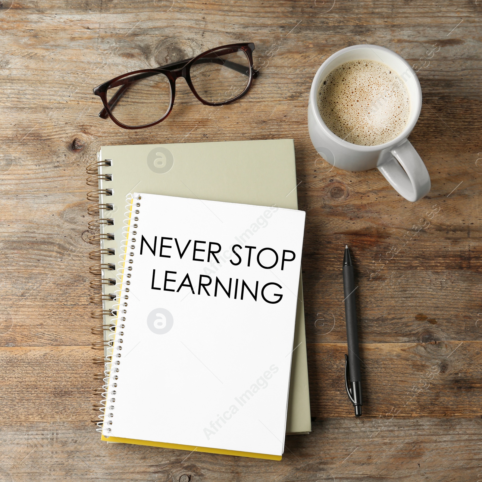 Image of Notebook with phrase NEVER STOP LEARNING, glasses and cup of coffee on wooden table, flat lay