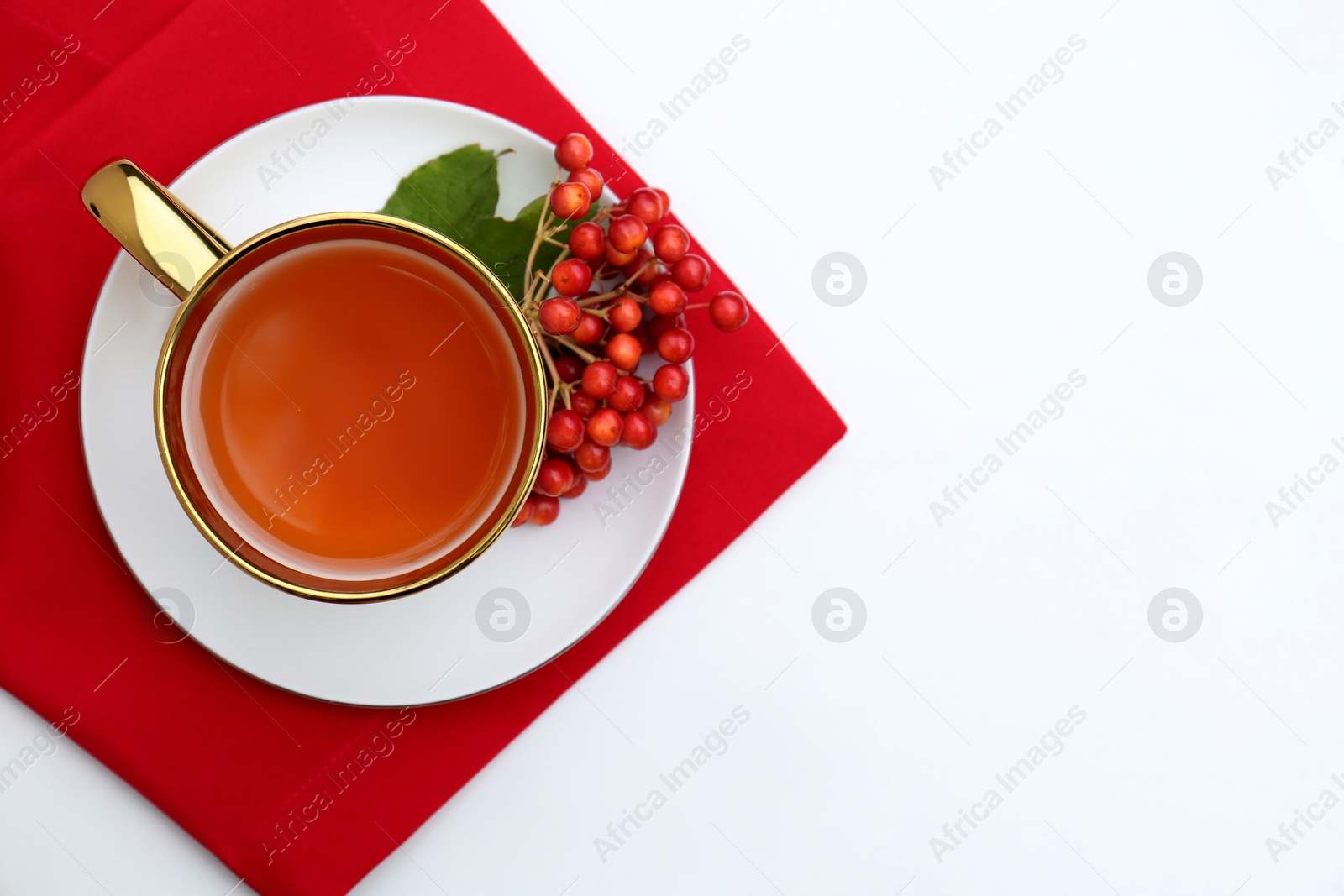 Photo of Cup of tea and fresh ripe viburnum berries on white table, top view. Space for text