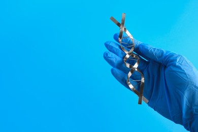 Scientist with DNA molecular chain model made of metal on blue background, closeup. Space for text