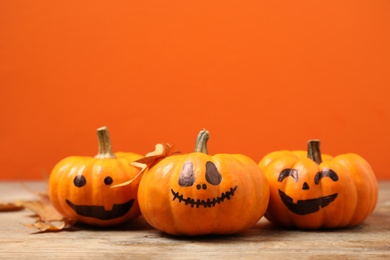 Photo of Pumpkins with scary faces and fallen leaves on orange background, space for text. Halloween decor