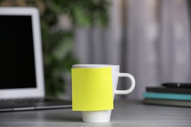 Cup with blank sticky note on white wooden table indoors. Space for text