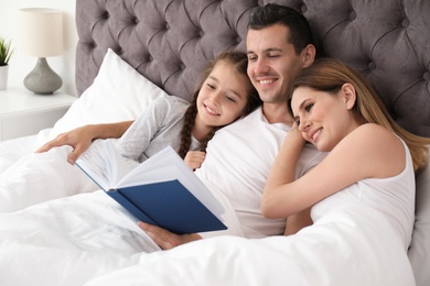 Photo of Happy family reading book with child in bedroom