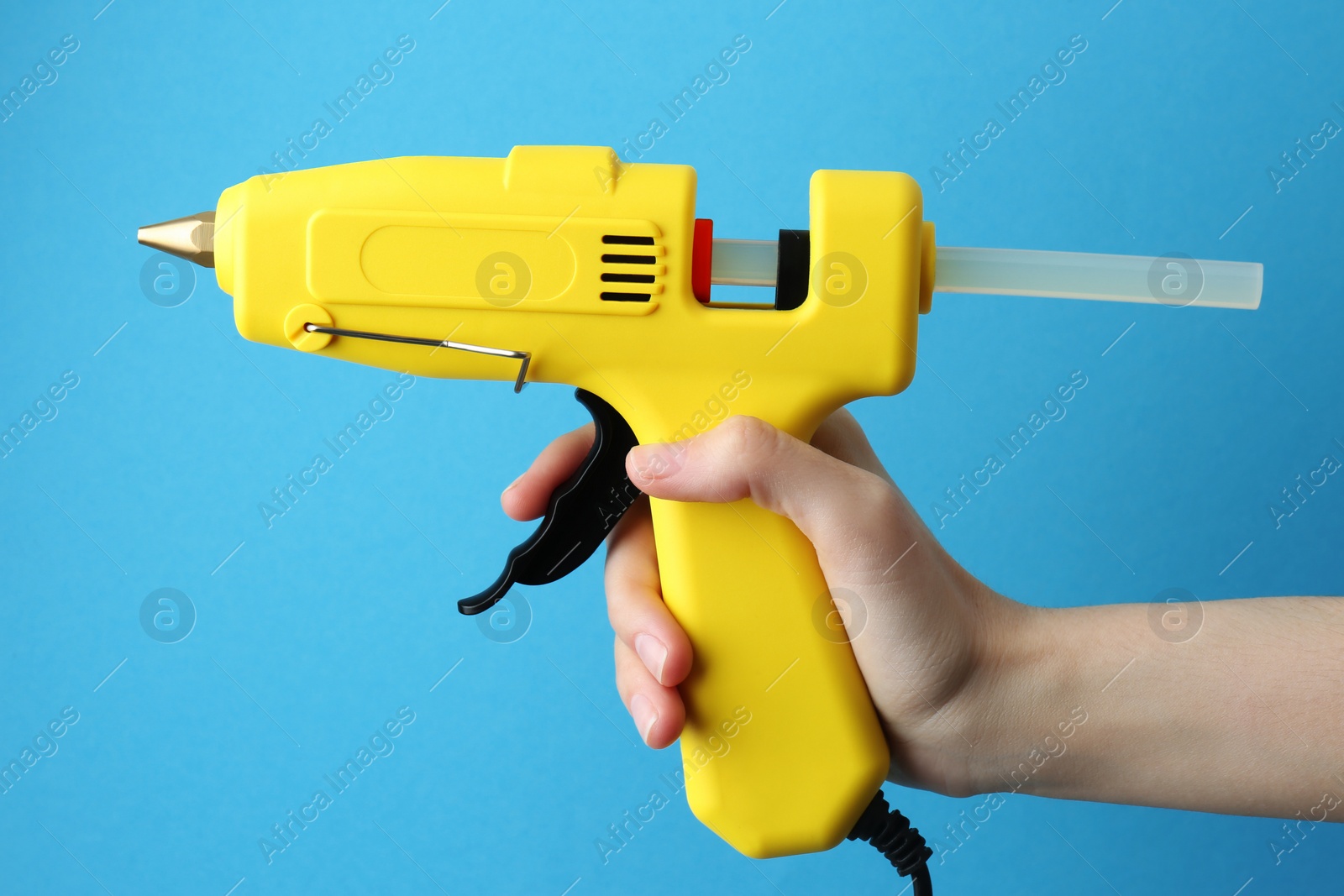 Photo of Woman holding yellow glue gun with stick on light blue background, closeup