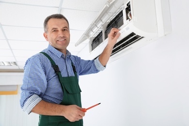 Electrician with screwdriver repairing air conditioner indoors