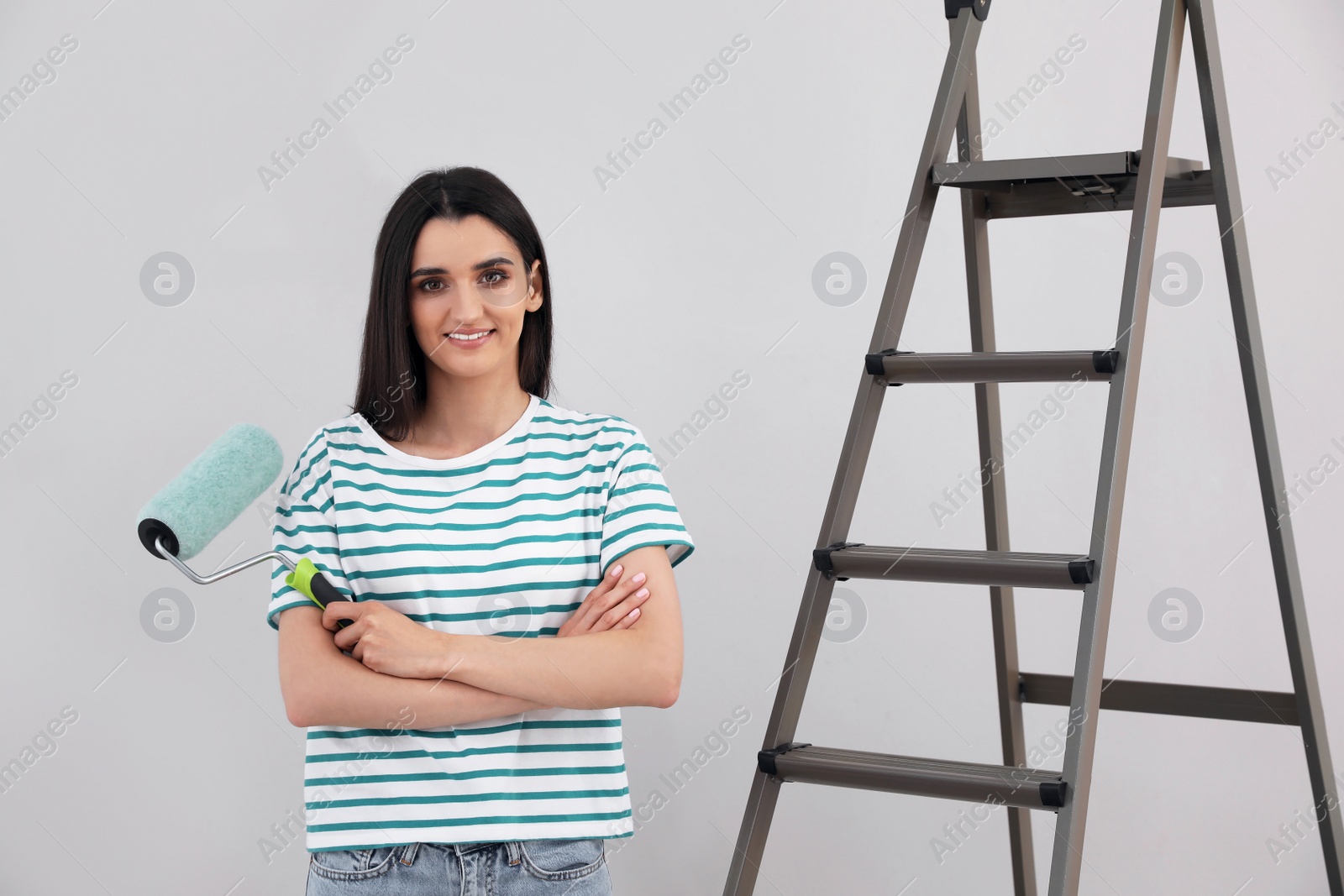 Photo of Young woman with roller and ladder near light wall