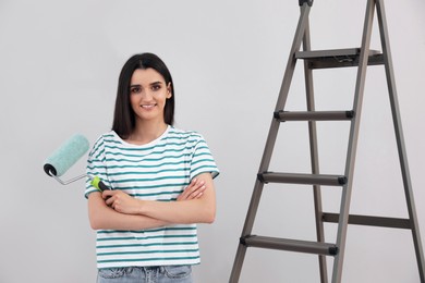 Young woman with roller and ladder near light wall
