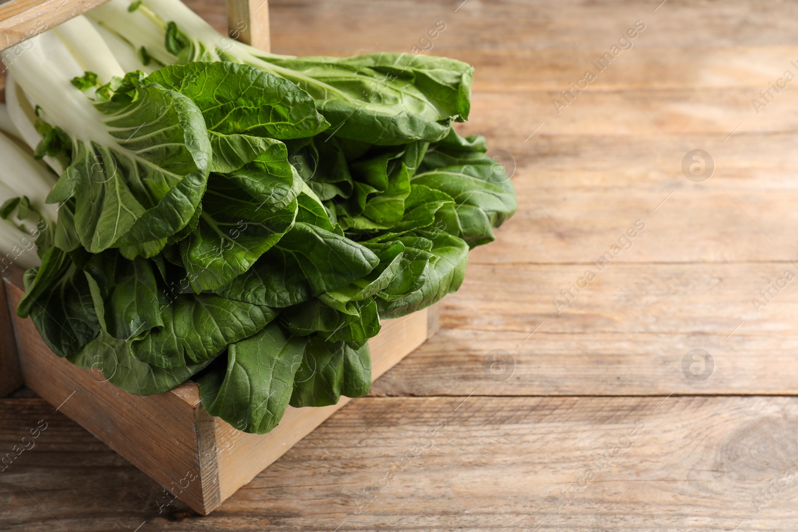 Photo of Fresh green pak choy cabbages in crate on wooden table, closeup. Space for text