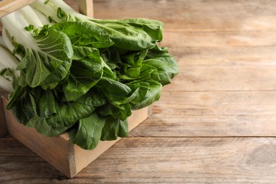 Photo of Fresh green pak choy cabbages in crate on wooden table, closeup. Space for text