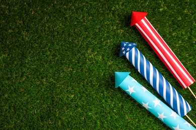 Photo of Firework rockets on green grass, flat lay. Space for text