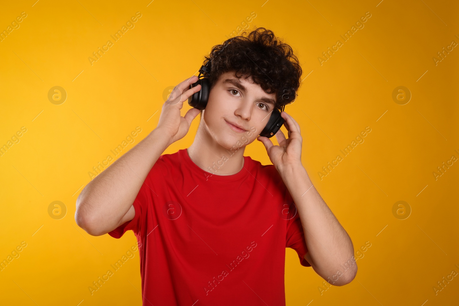Photo of Portrait of teenage boy listening music with headphones on orange background