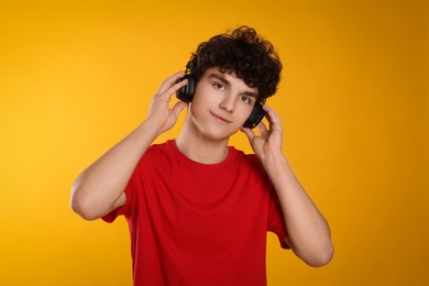 Portrait of teenage boy listening music with headphones on orange background