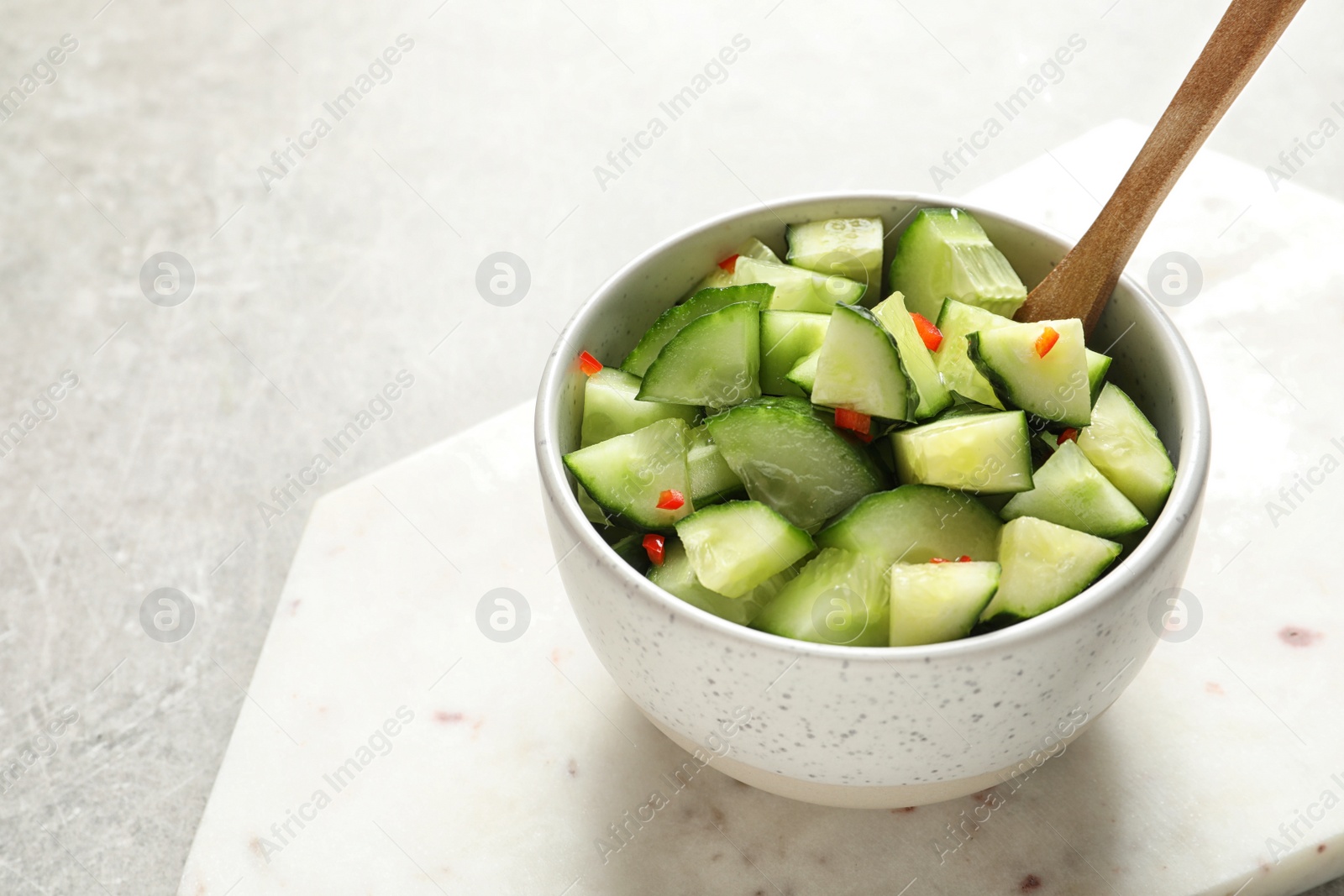 Photo of Delicious cucumber salad in bowl with board on grey table. Space for text