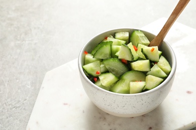 Photo of Delicious cucumber salad in bowl with board on grey table. Space for text