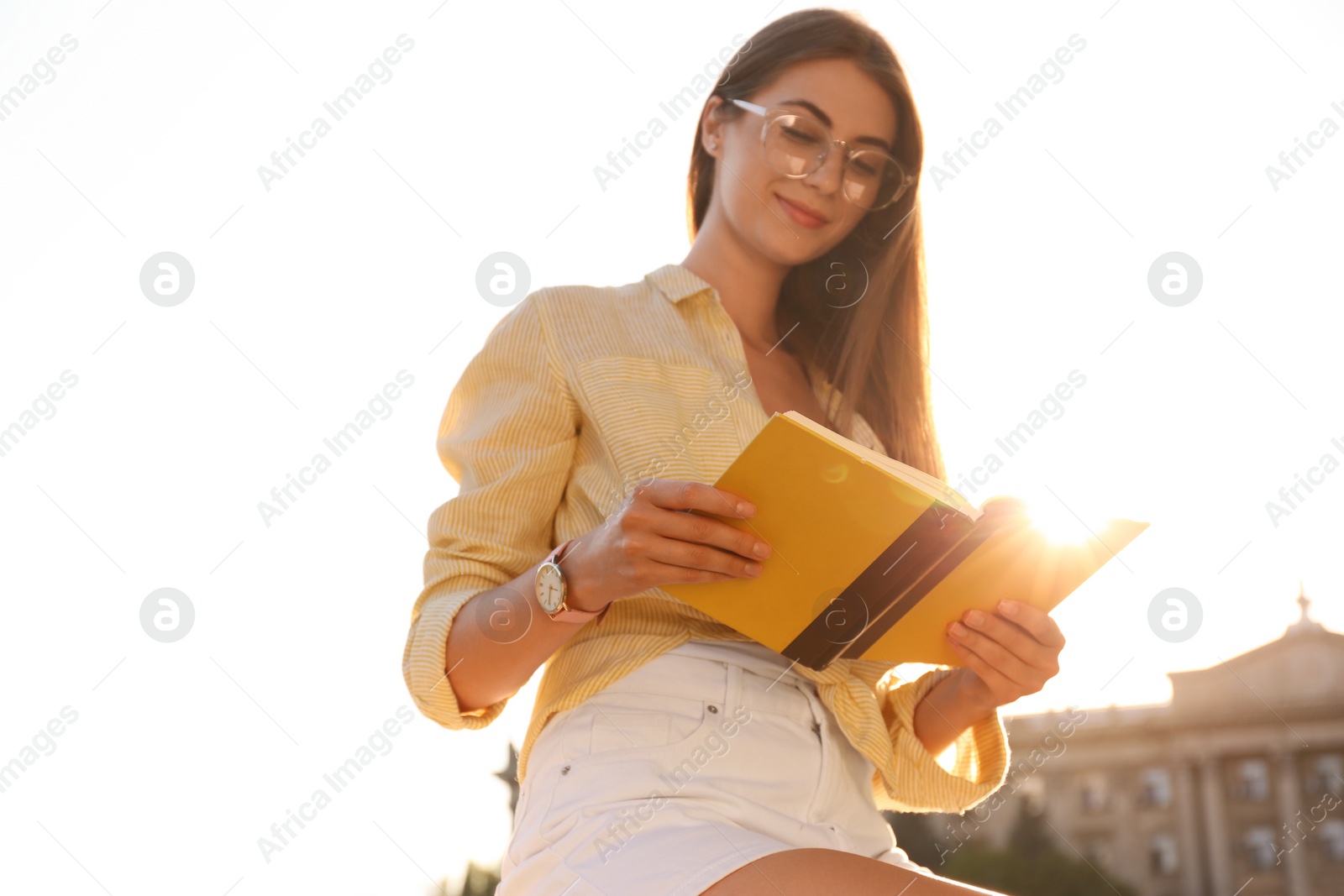 Photo of Young woman reading book outdoors on sunny day