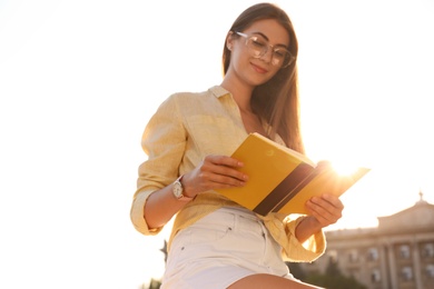 Photo of Young woman reading book outdoors on sunny day