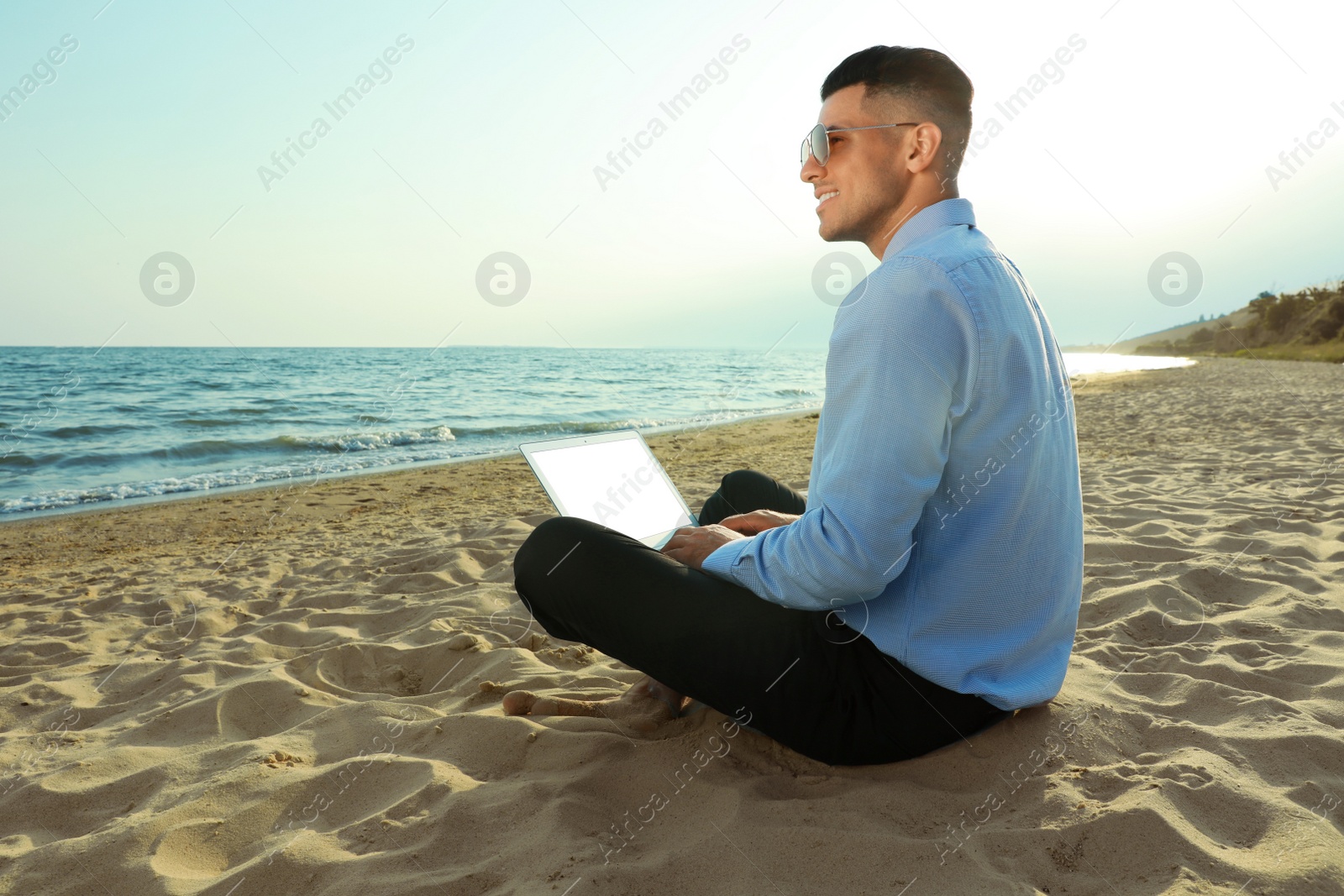 Photo of Happy businessman working with laptop on beach. Business trip