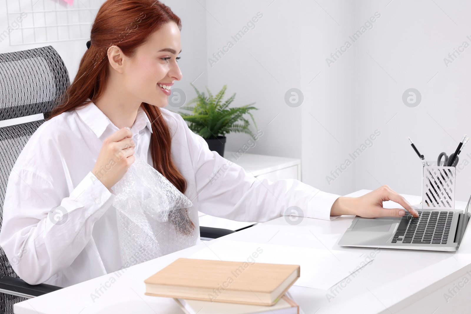 Photo of Woman popping bubble wrap at desk in office. Stress relief