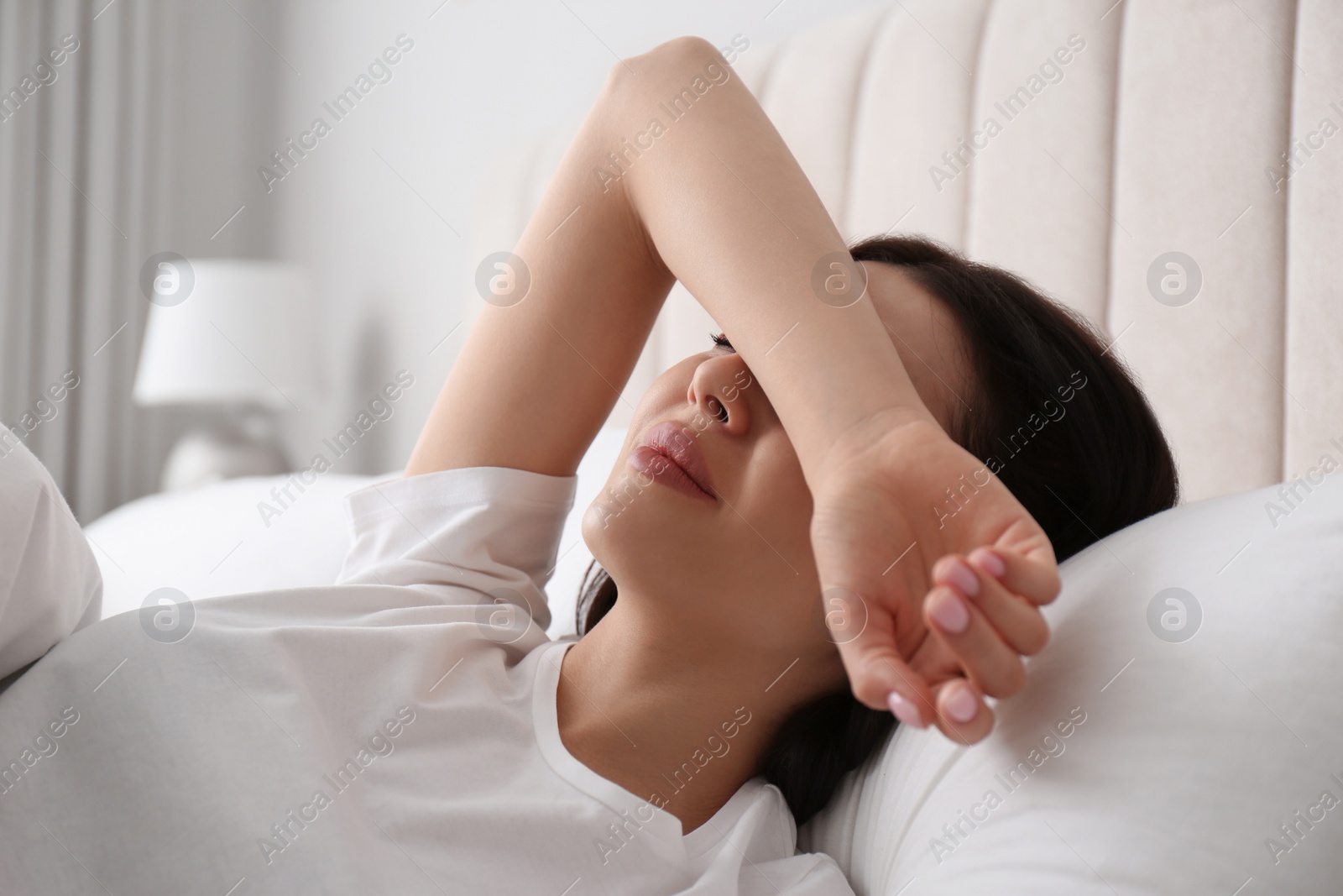 Photo of Young woman suffering from migraine in bed at home