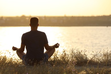 Photo of Man meditating on hill near river at sunset, back view. Space for text