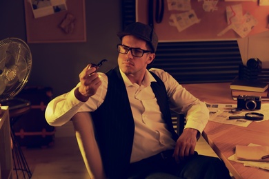 Photo of Old fashioned detective with smoking pipe at table in office