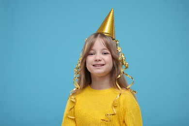 Photo of Happy little girl in party hat on light blue background