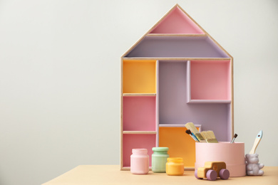 Photo of Composition with house shaped shelf and jars of paints on table, space for text. Interior element