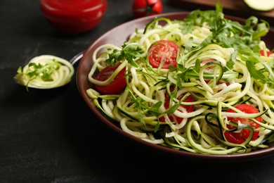 Photo of Delicious zucchini pasta with arugula and cherry tomatoes on black slate table, closeup